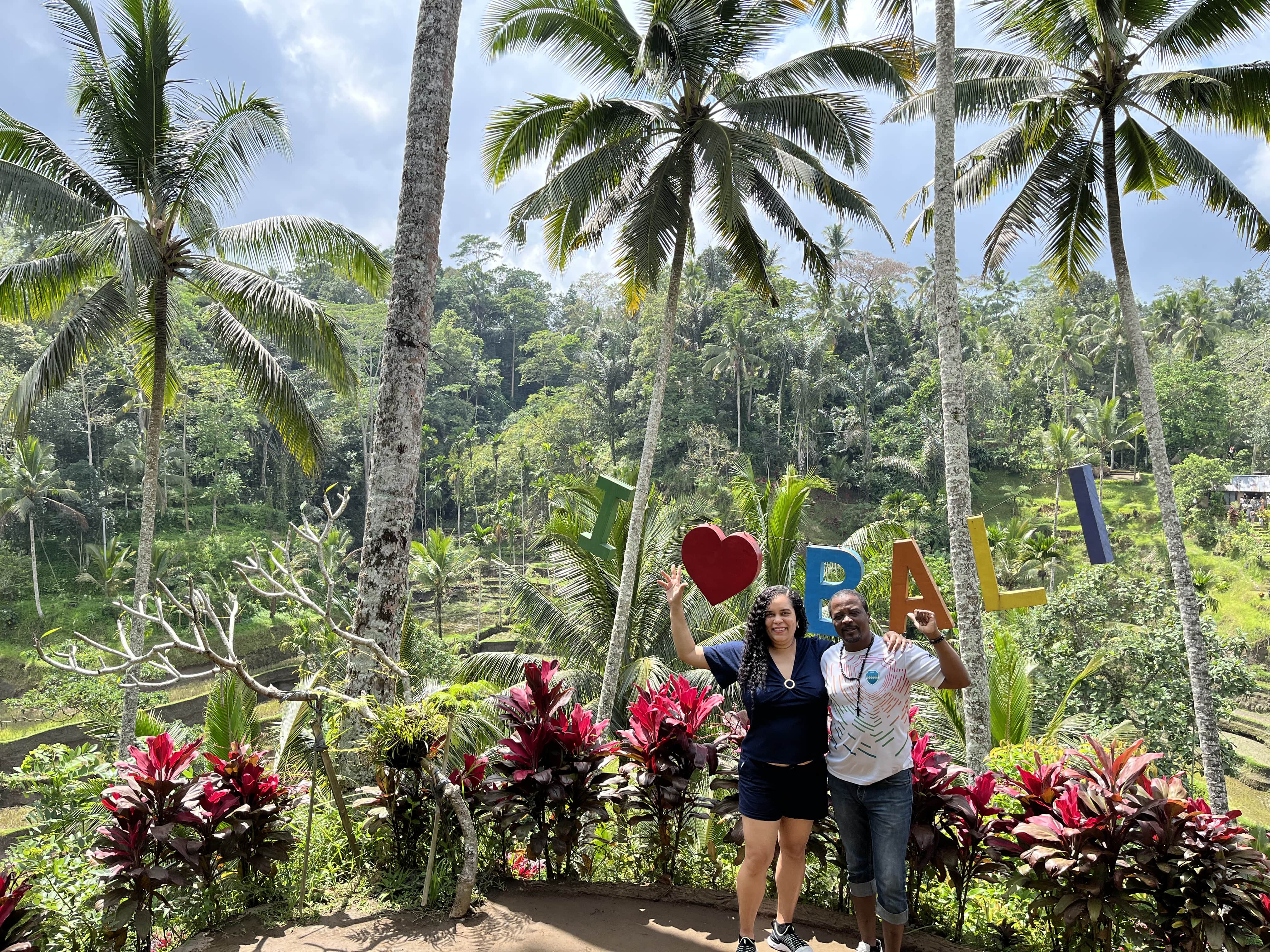 Caroline and Pedro smiling in front of an 'I Love Bali' sign with rice paddies in the background