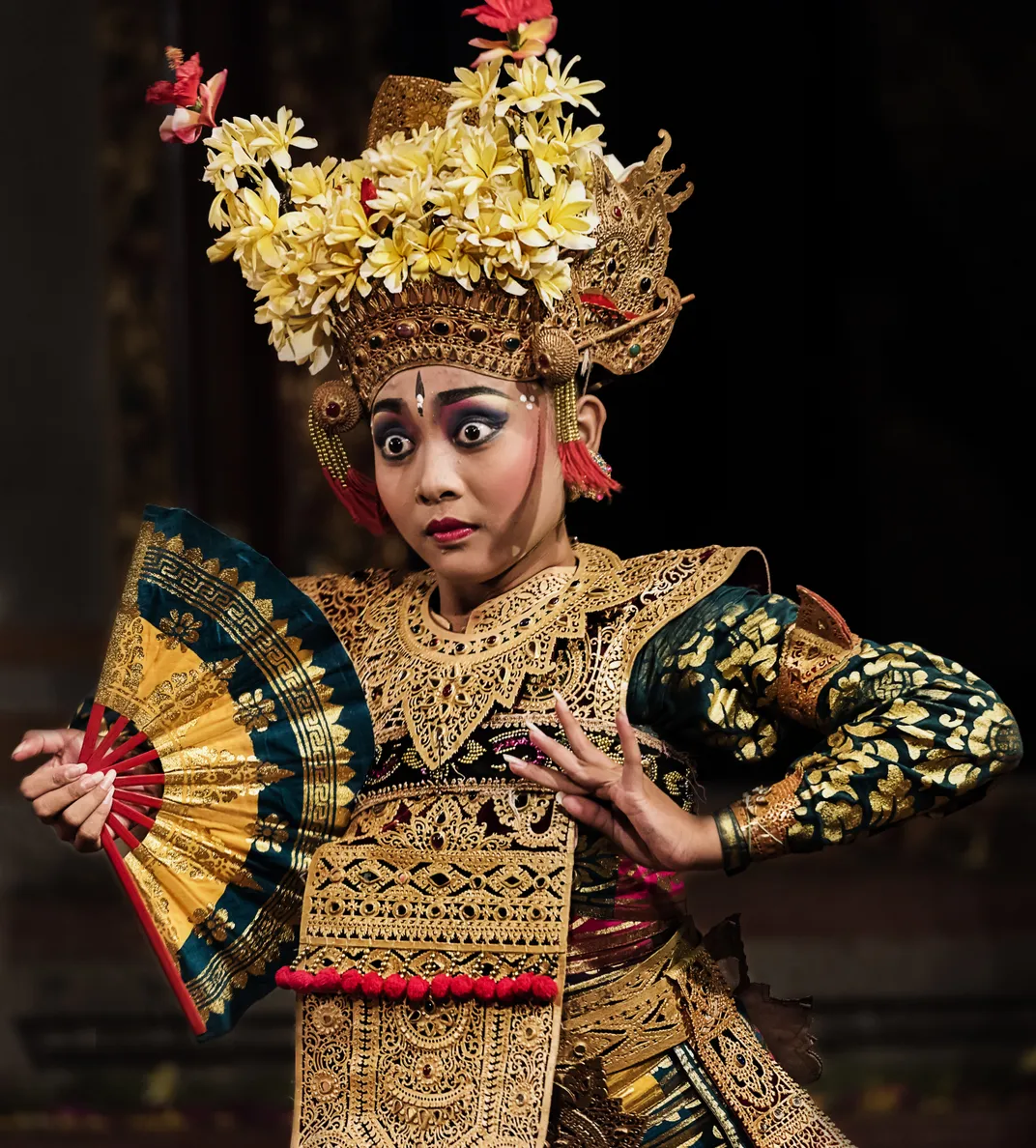 Traditional Balinese dancer in elaborate golden costume performing with decorative fan