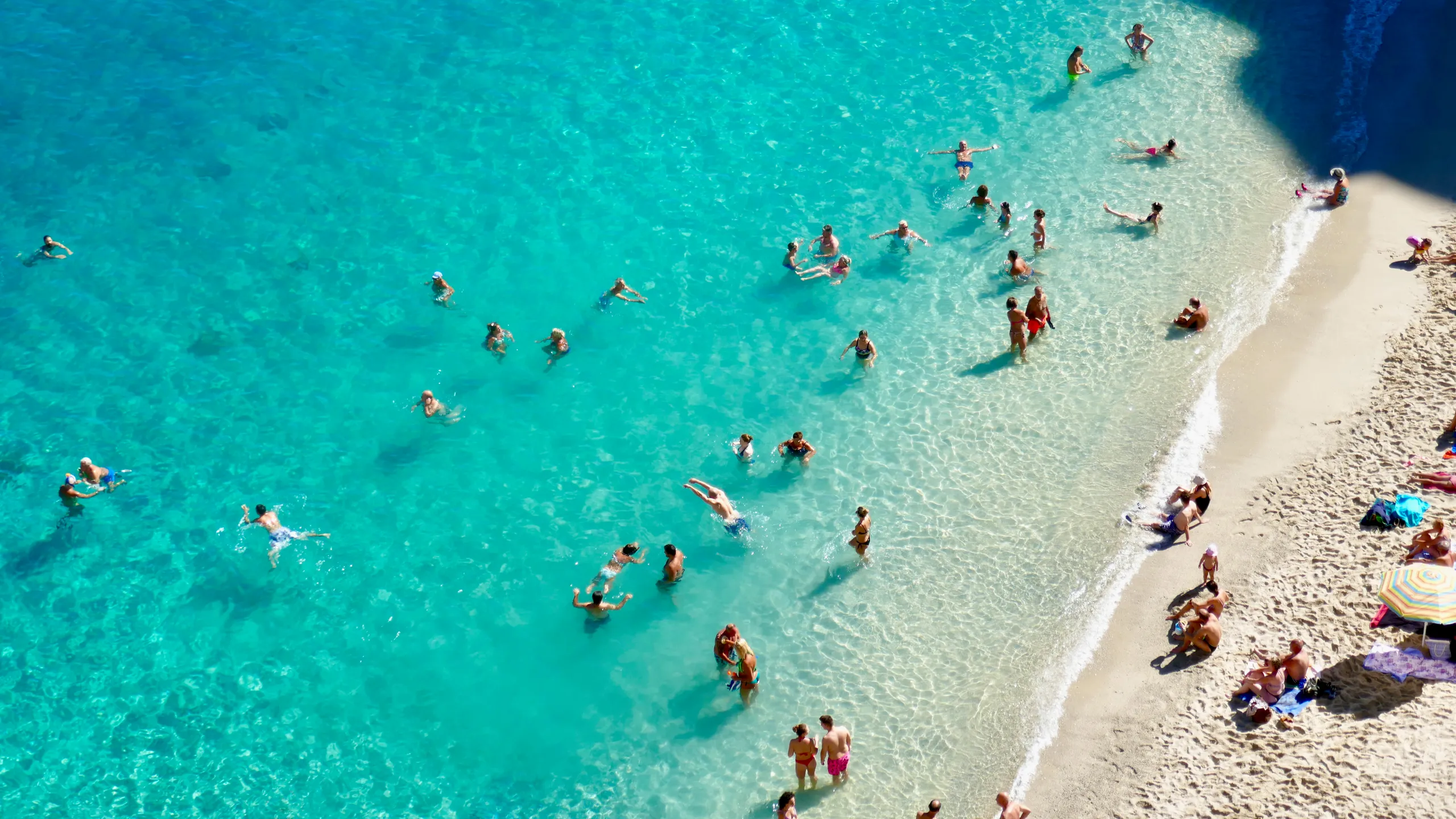 Aerial view of pristine tropical beach with crystal clear turquoise water and people enjoying swimming and beach activities